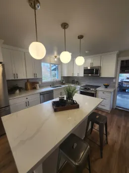 Modern kitchen with white cabinets, island, globe pendant lights, and stools.