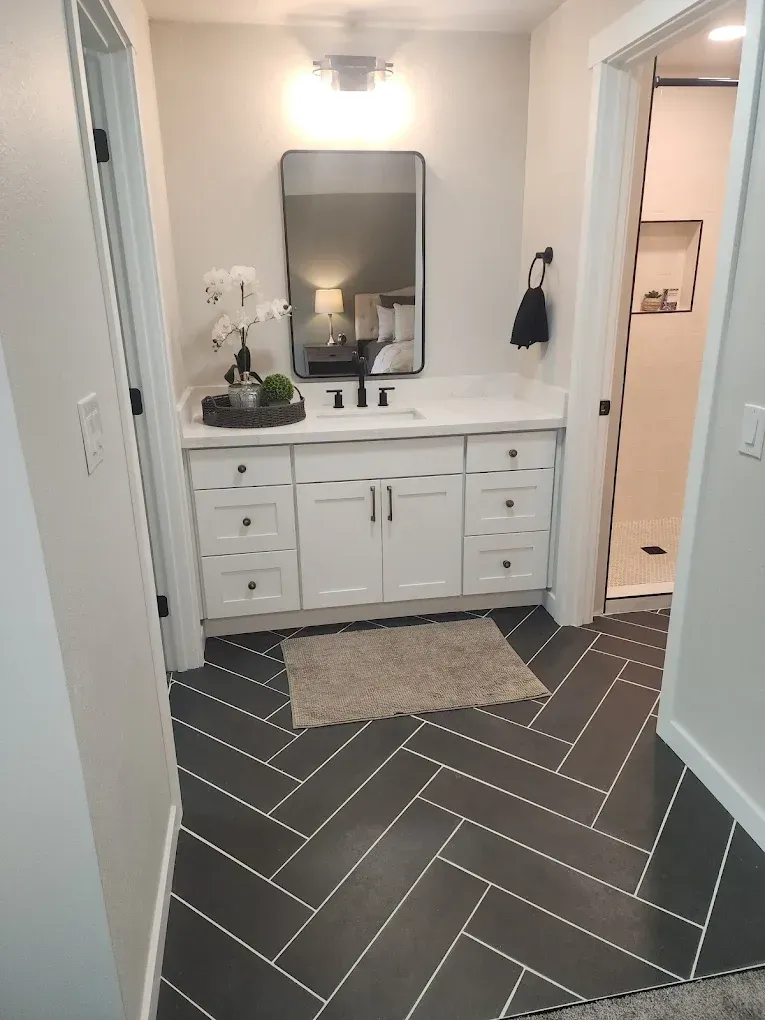 Bathroom with white vanity, black herringbone tile floor, and a doorway to the shower.