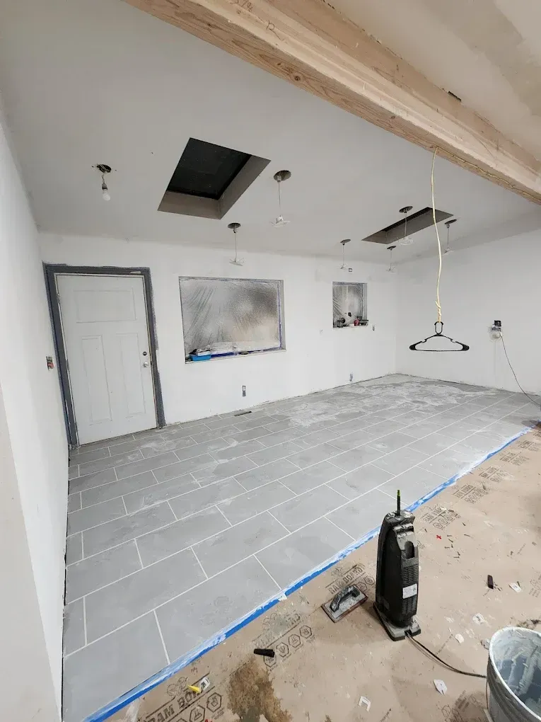 Room under renovation: gray tiled floor, white walls, door, windows, skylights.