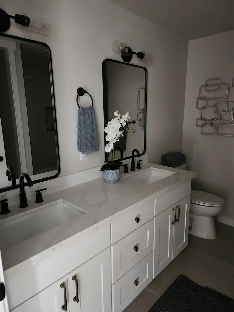 Bathroom with white double vanity, black fixtures, rectangular mirrors, and a white orchid.