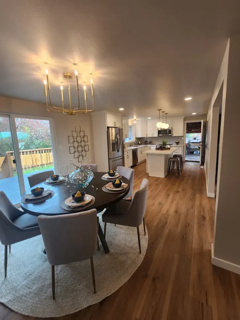 Dining room with round table set for guests, open to kitchen and backyard.
