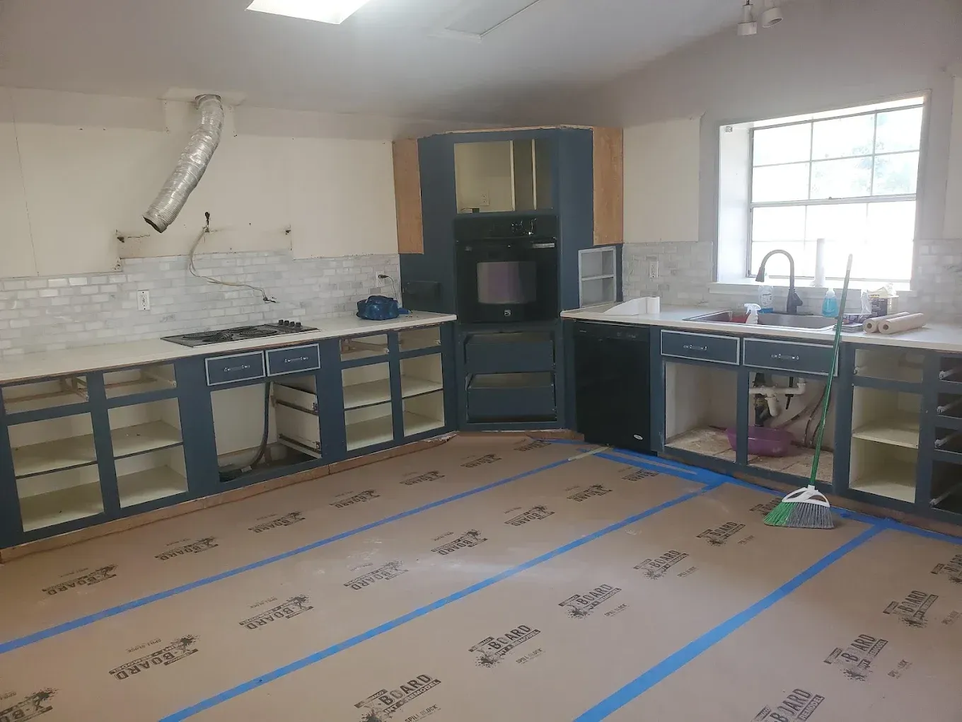 Kitchen renovation: blue cabinets, countertops, oven, and sink. Floor is covered with protective paper.