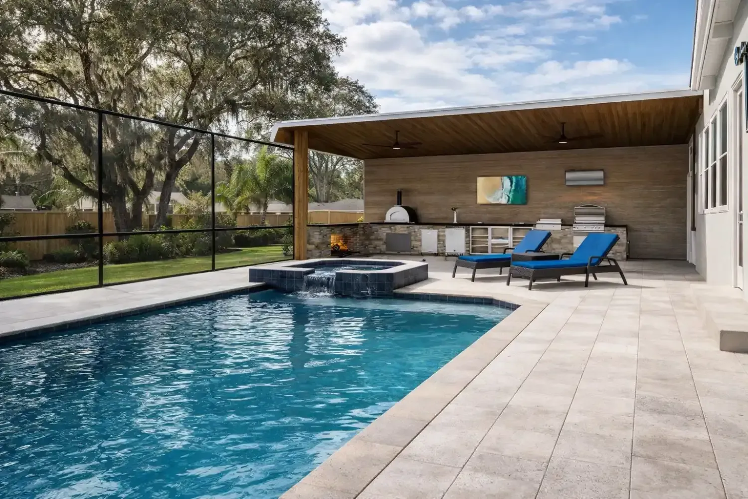 A blue backyard swimming pool with a spa feature next to a covered patio with lounge chairs and an outdoor kitchen.