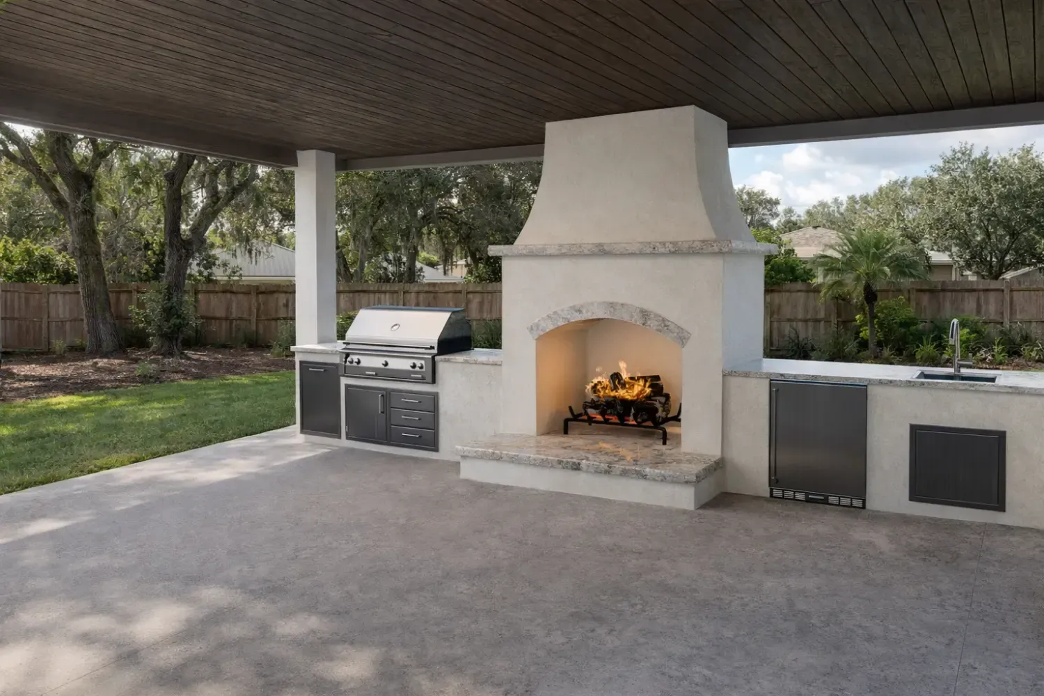 An outdoor patio featuring a central stucco fireplace, a built-in stainless steel grill, and a covered ceiling.
