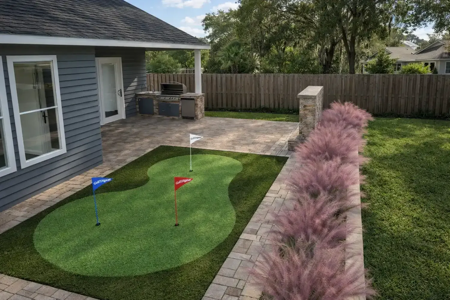 A backyard putting green with three golf flags next to a stone patio and a row of pink Muhly grass against a wooden fence.