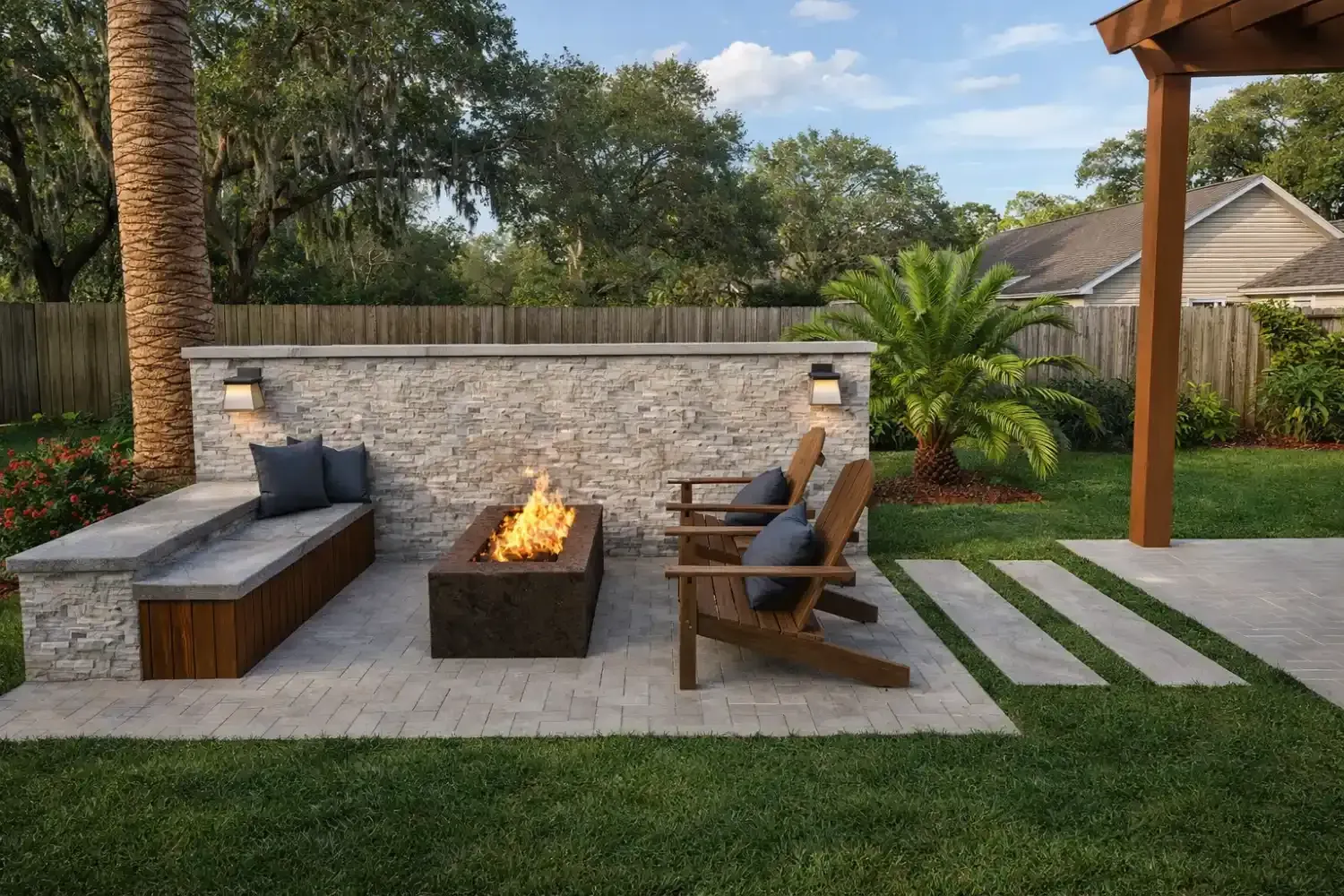 Backyard patio with stone fire pit, built-in bench, and wooden chairs, surrounded by grass and landscaping.