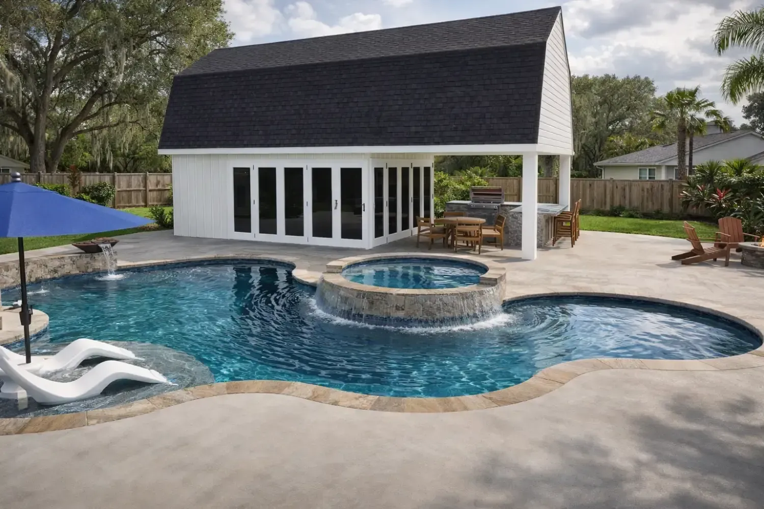 Backyard pool with a built-in spa, white pool house, lounge chairs, and a blue umbrella on a sunny day.