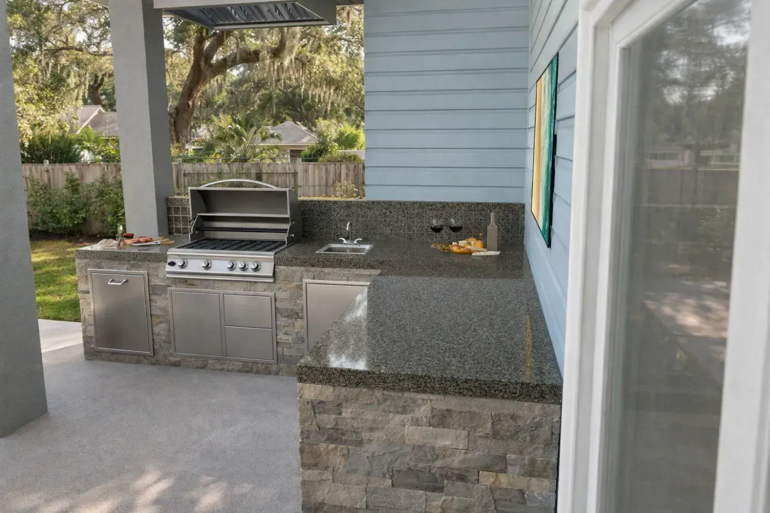 An outdoor kitchen with a stainless steel grill, a small sink, and dark granite countertops set against a blue wall.