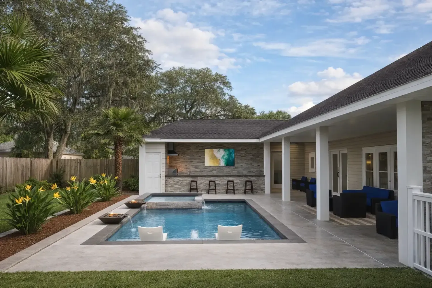 A backyard with a rectangular swimming pool, integrated spa, covered patio, bar seating, and lush landscaping.