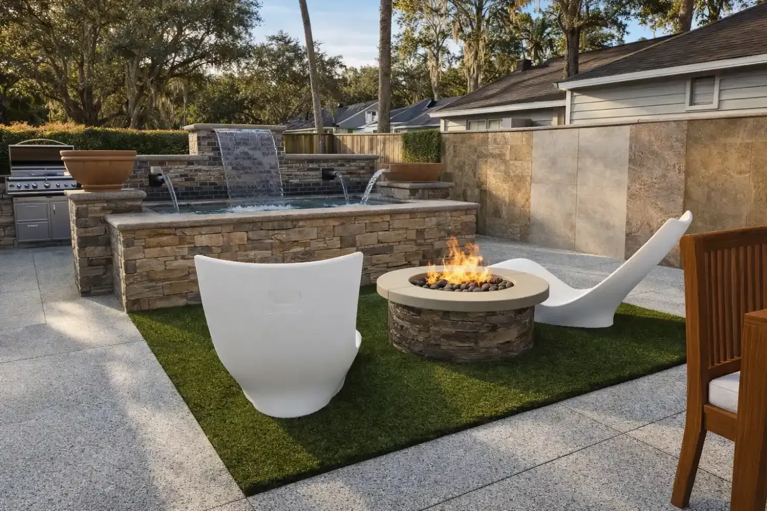 Outdoor patio with a stone fire pit, white modern lounge chairs on artificial turf, and a stone water feature.