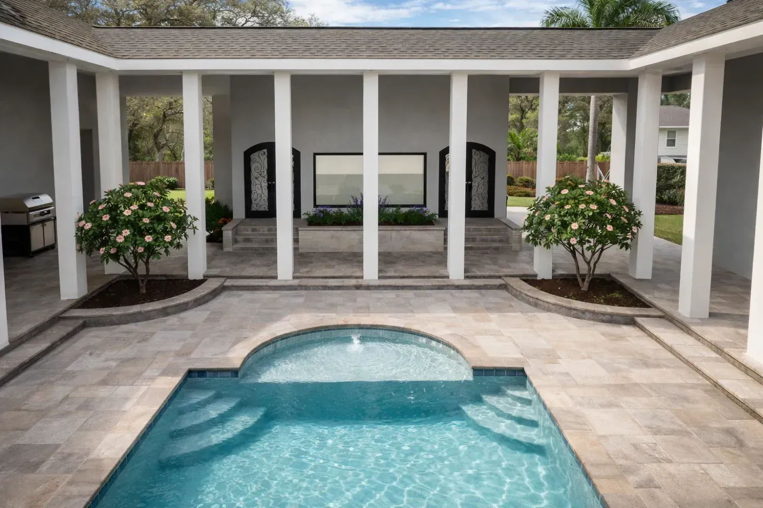 A courtyard pool with travertine pavers, two flowering trees, and a covered colonnade surrounding the patio.