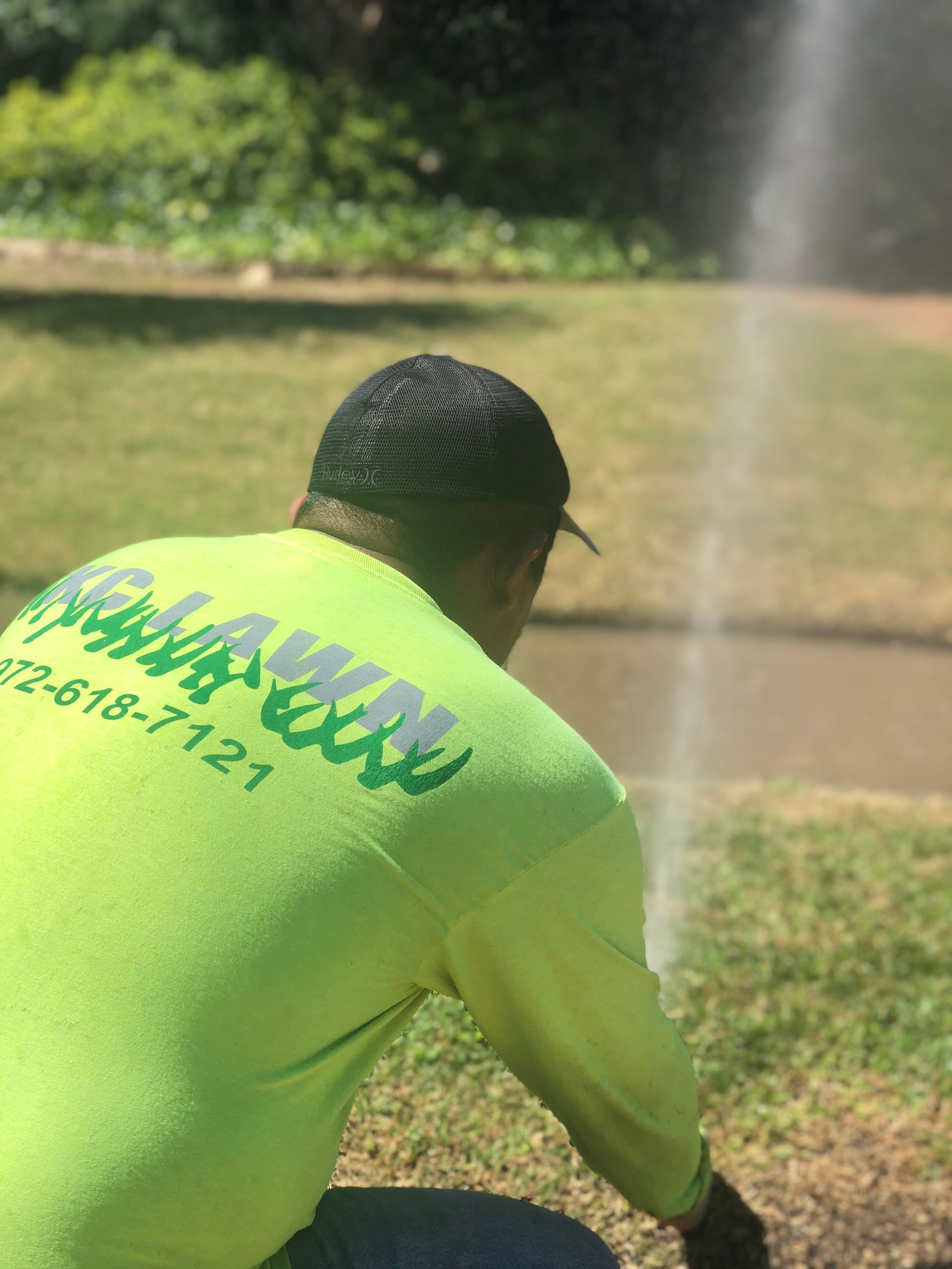 Man in green shirt inspecting sprinkler system on a lawn. Light green shirt with 