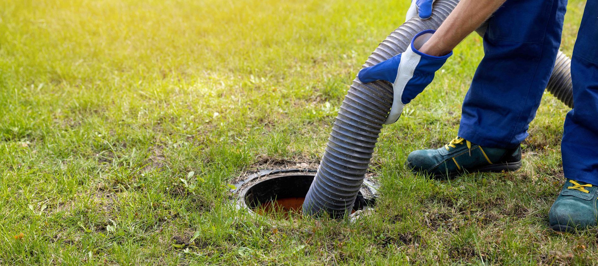 A man is pumping a septic tank using a large vacuum hose inserted into the ground.