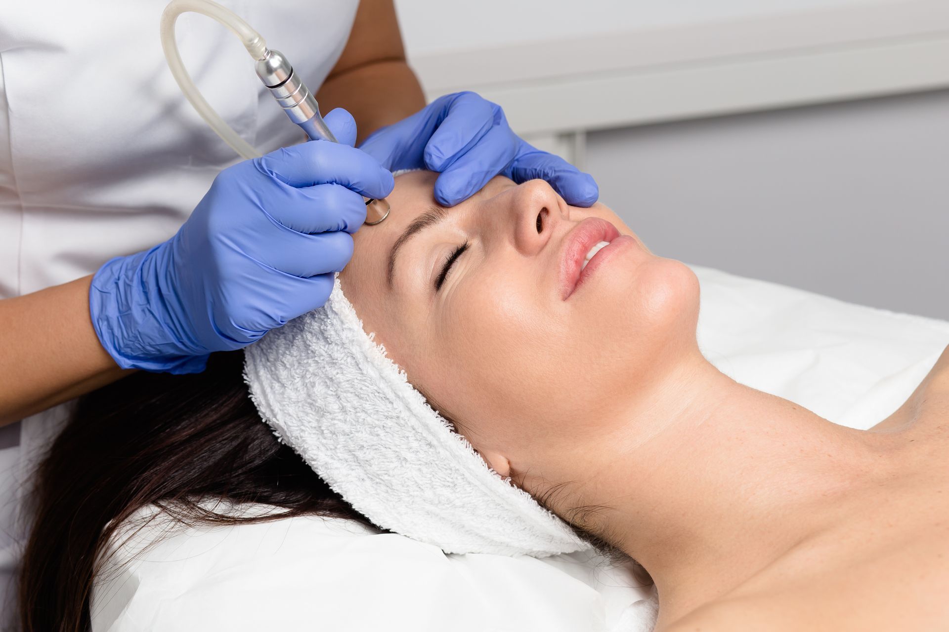 Esthetician performing a facial treatment with a microdermabrasion device in a spa setting.