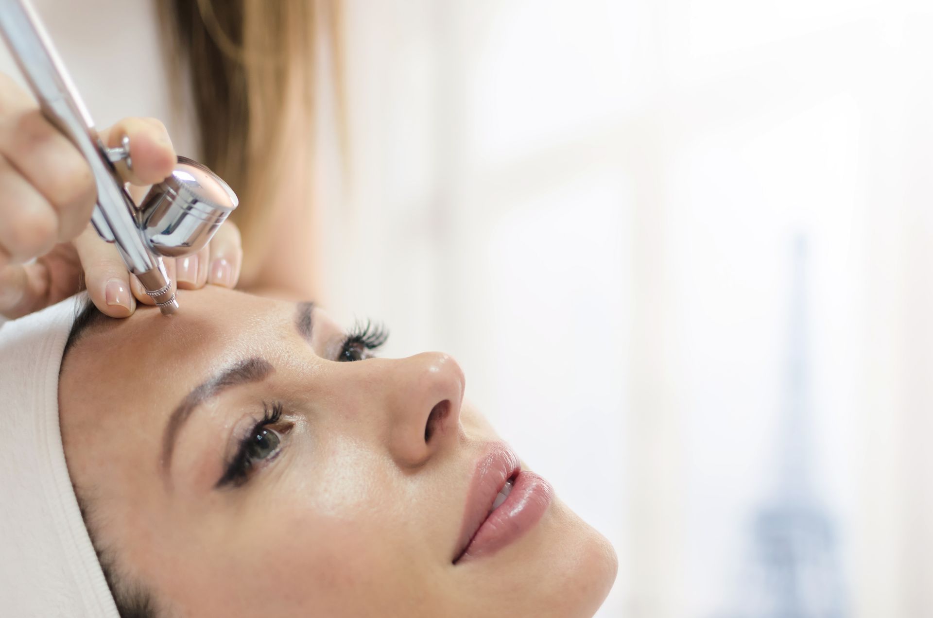 Airbrush makeup application with professional tool in bright studio setting.