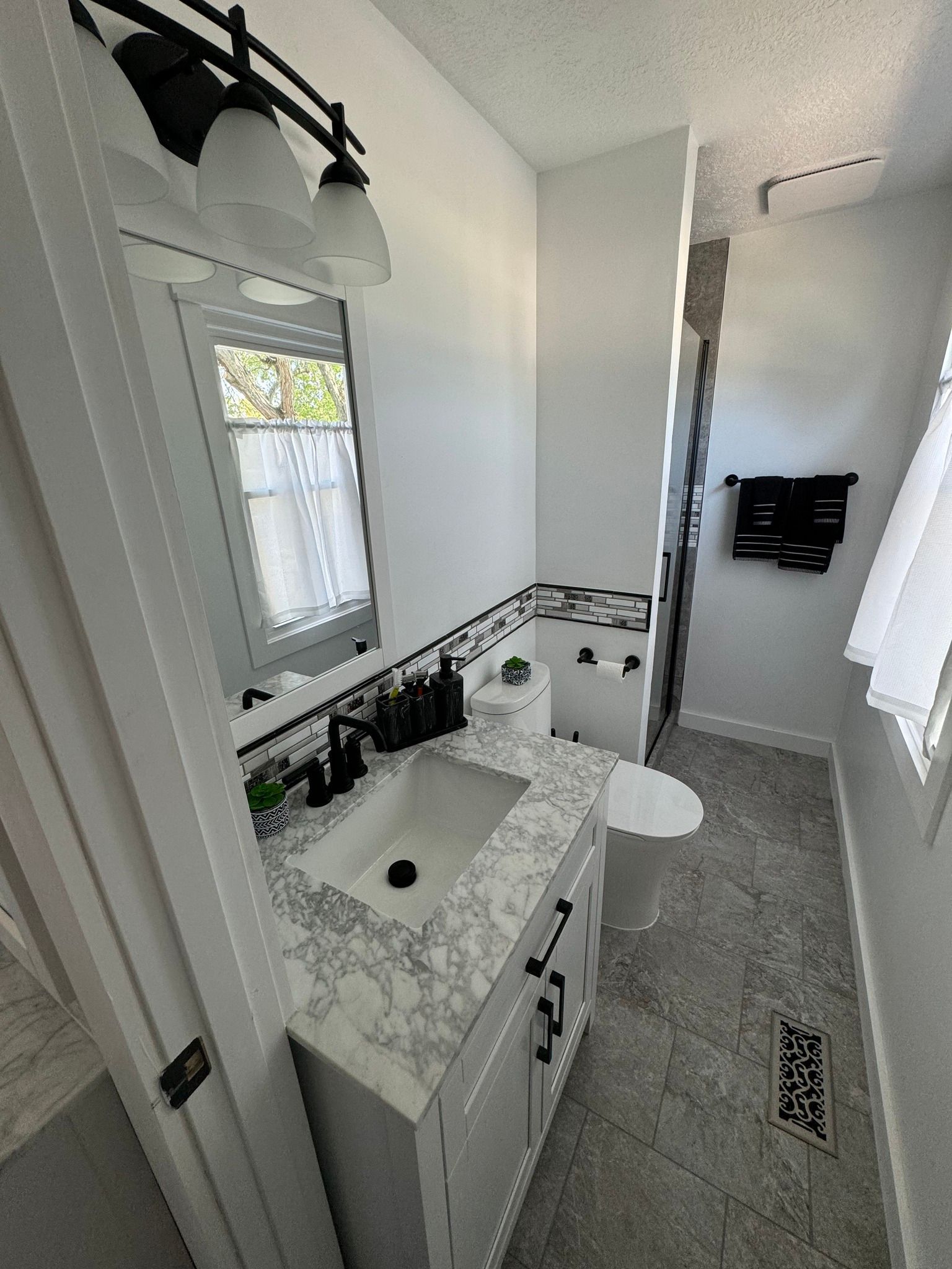 Bathroom with white vanity, marble countertop, black fixtures, and tiled floor.
