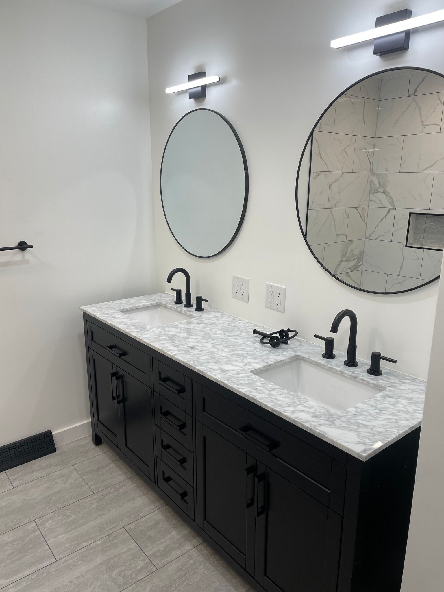 Bathroom with black vanity, white countertop, round mirrors, and black faucets.