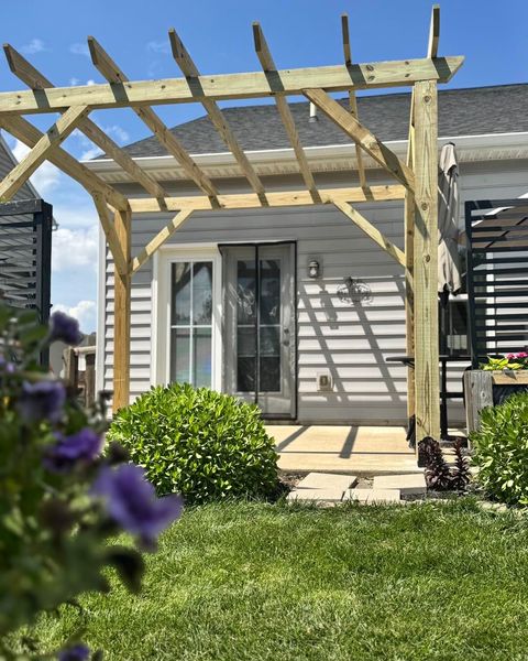 Wooden pergola over a doorway, with blue sky and green yard.