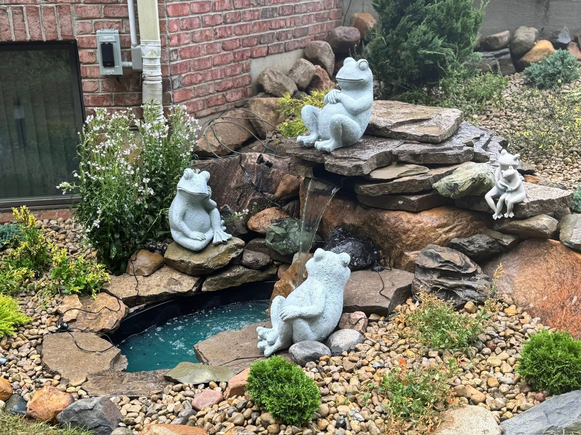 A small rock waterfall with multiple frog statues. The water flows into a small pond.