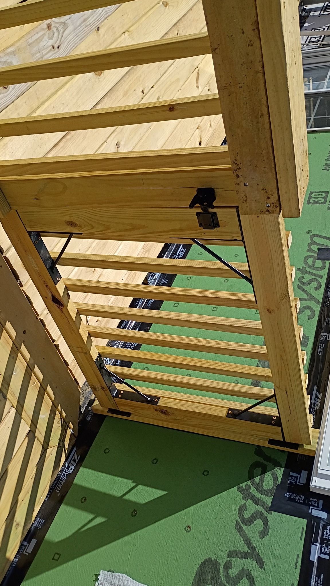 Wooden pergola under construction, green roofing material visible.