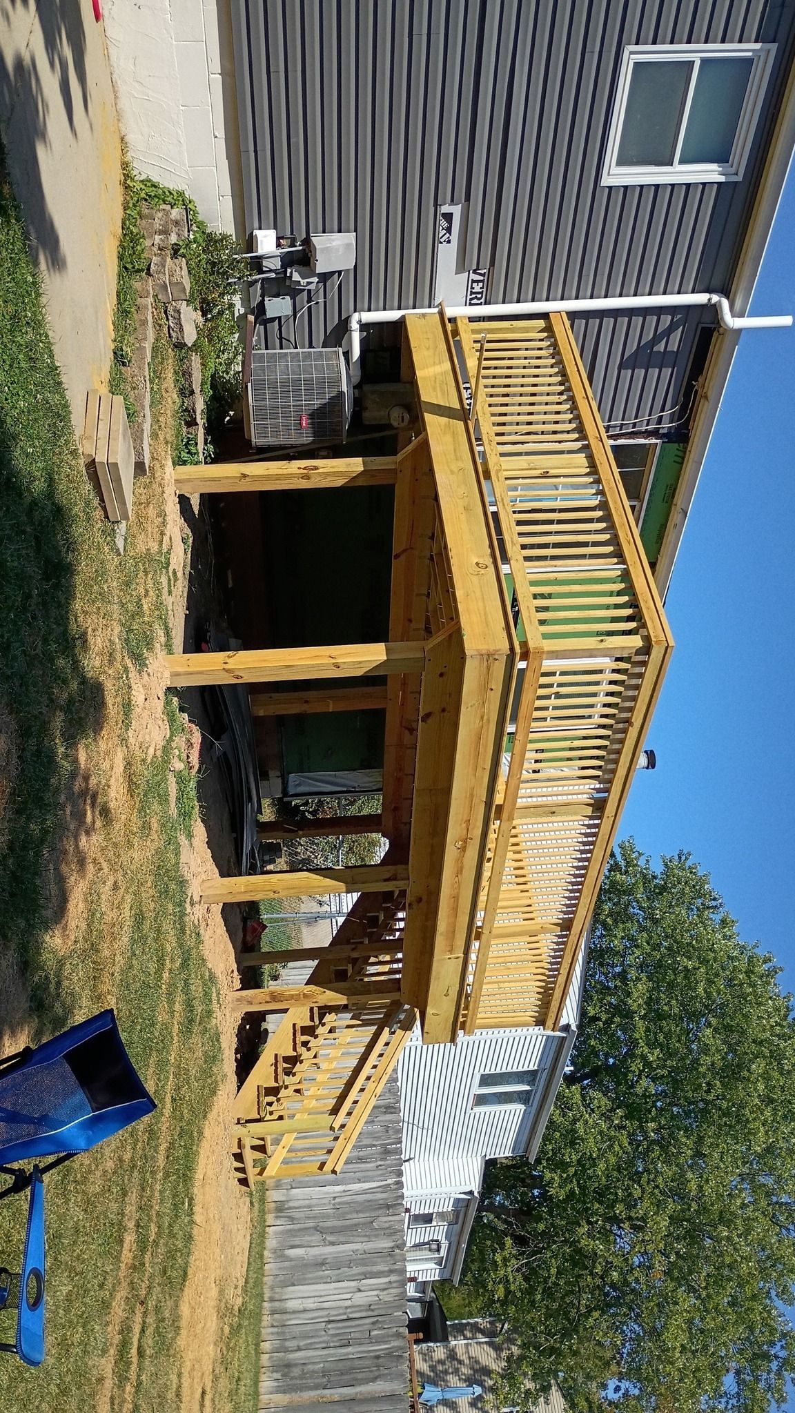 Wooden deck attached to a house with steps leading down to a yard; blue sky.