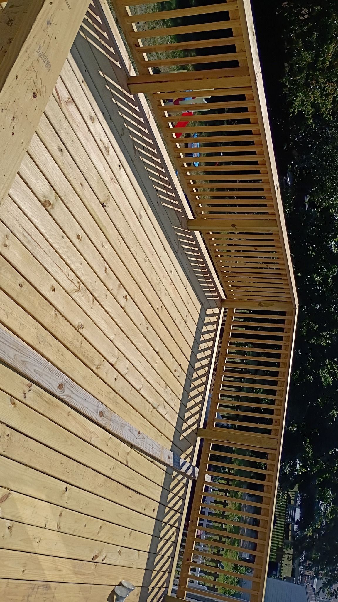 Wooden deck with railing casting a shadow; angled perspective.