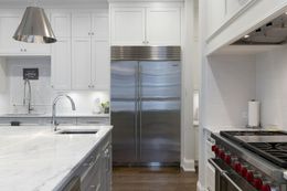 Stainless steel refrigerator flanked by white cabinets in a modern kitchen with marble countertops.