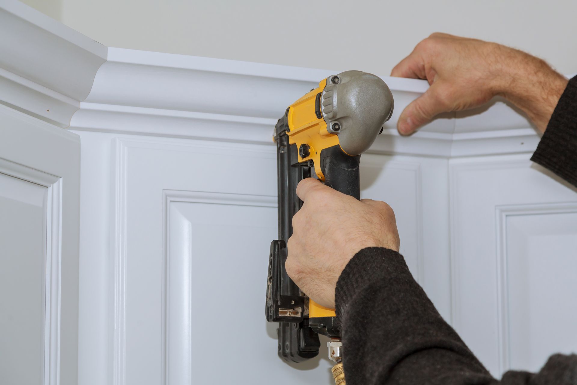 Person using a nail gun to install white crown molding on a white cabinet.