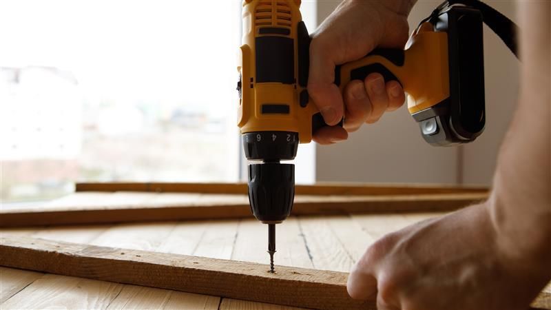 Person using a yellow drill to screw into a wooden board.