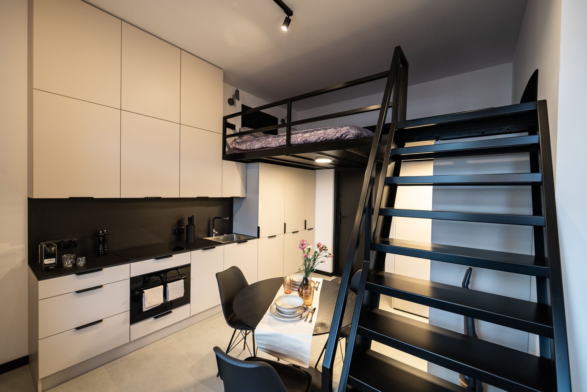 Small modern apartment with a loft bed, kitchen, dining area. Black and white color scheme.