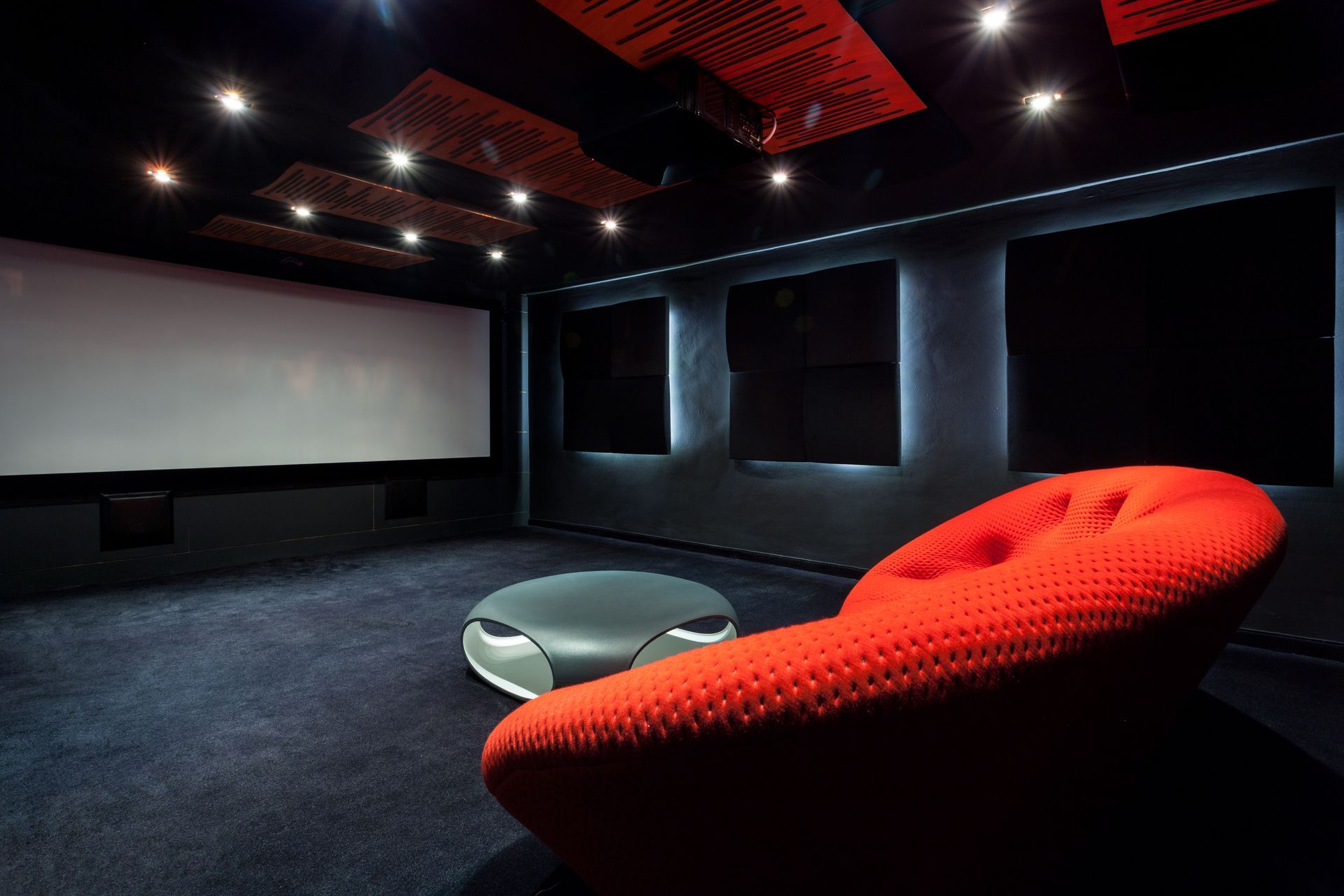 Red chair in a home theater room with a white screen, dark walls, and acoustic panels.