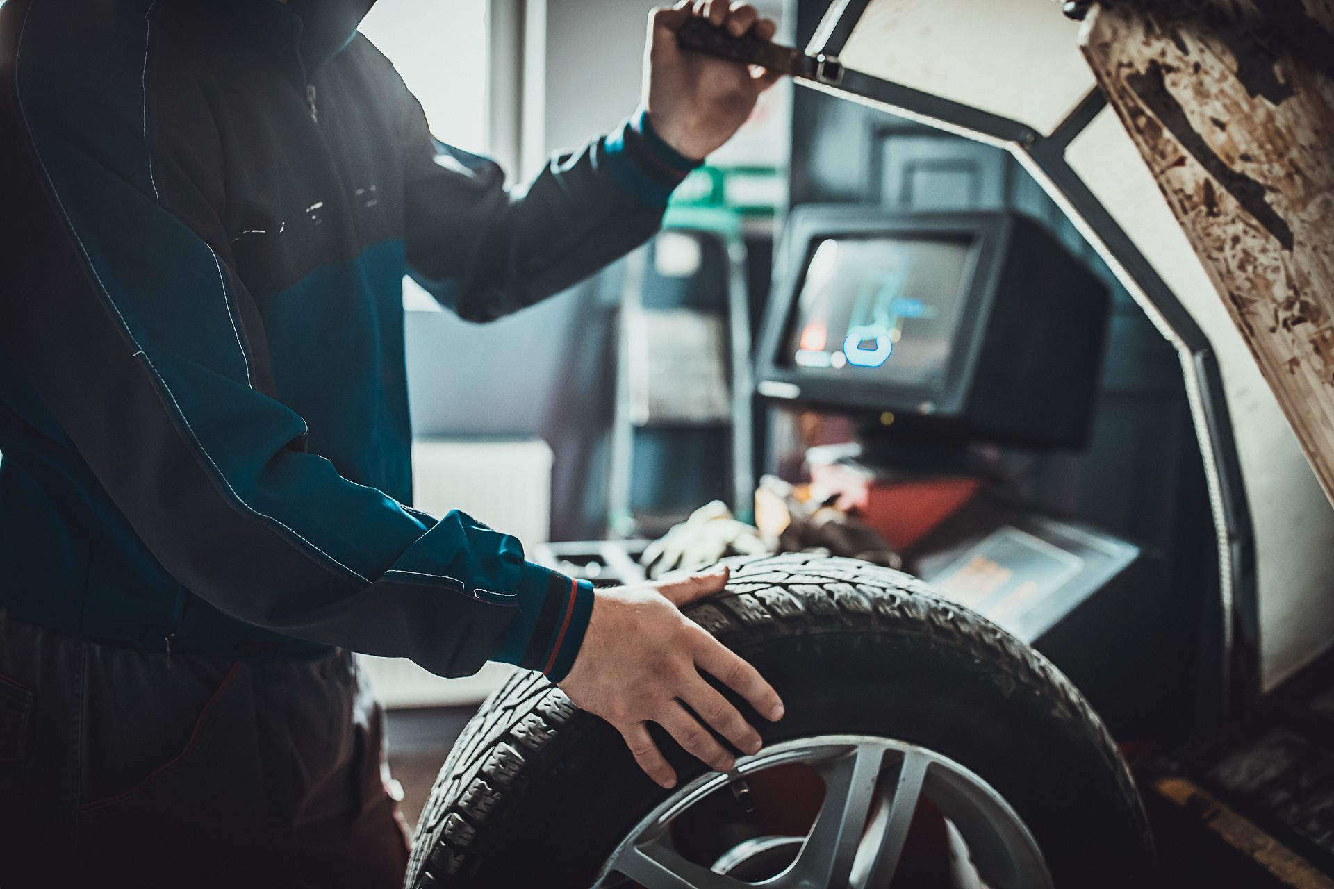 A man is balancing a tire on a machine in a garage.