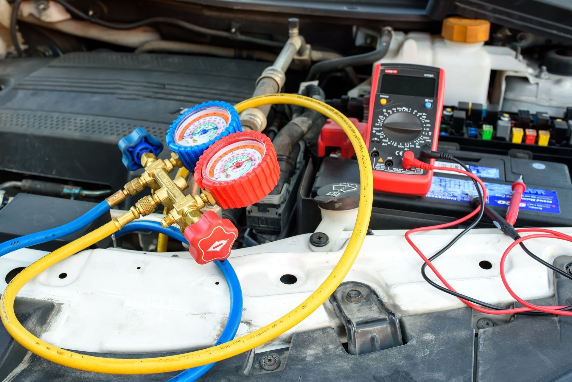 A car is being serviced with gauges and a multimeter.