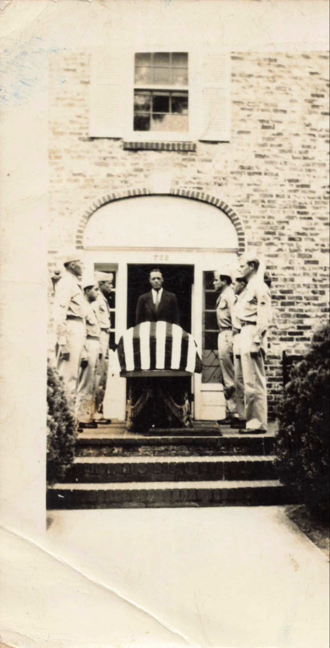 Men carry a striped casket from a brick building. One man stands in the doorway.