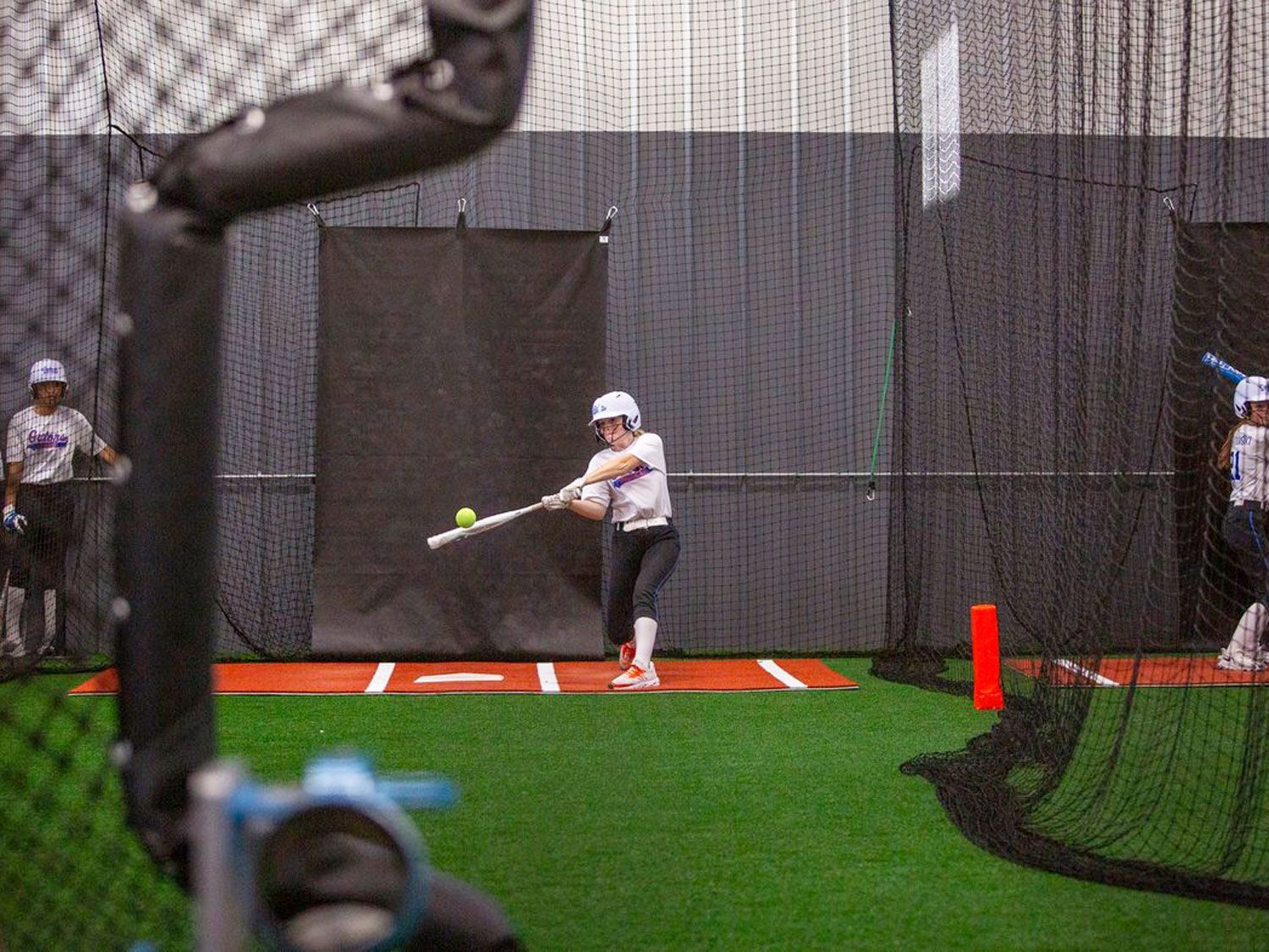 A softball player is swinging a bat at a ball in a cage.