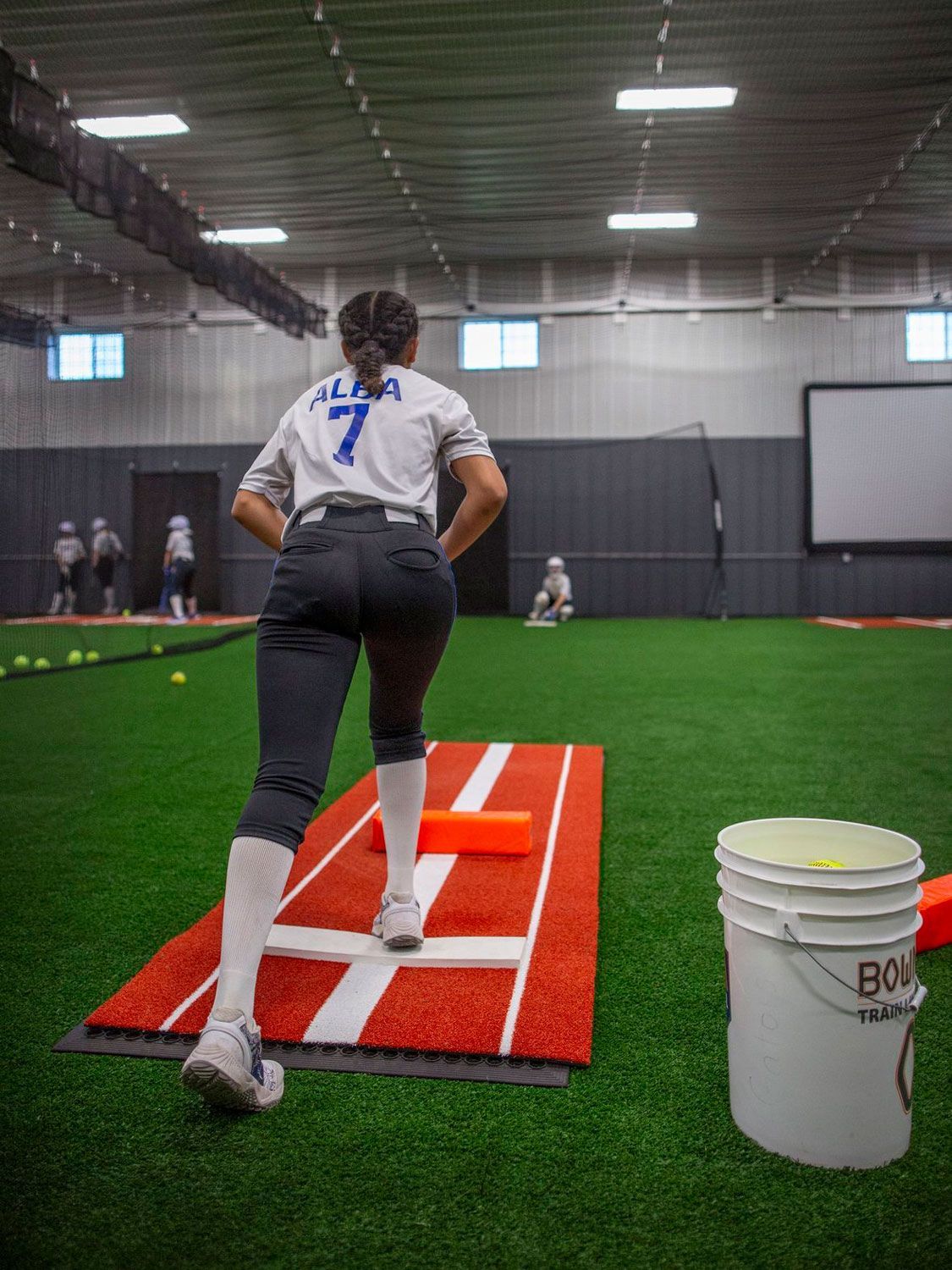 A woman in a number 7 jersey is pitching on a track.