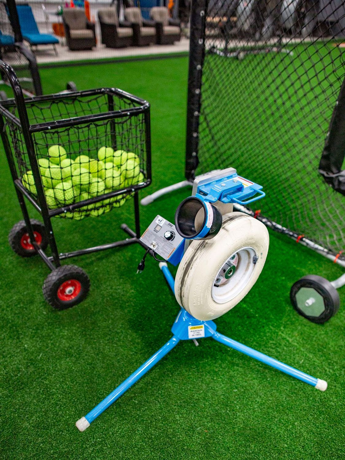 A pitching machine is sitting next to a cart filled with softballs.