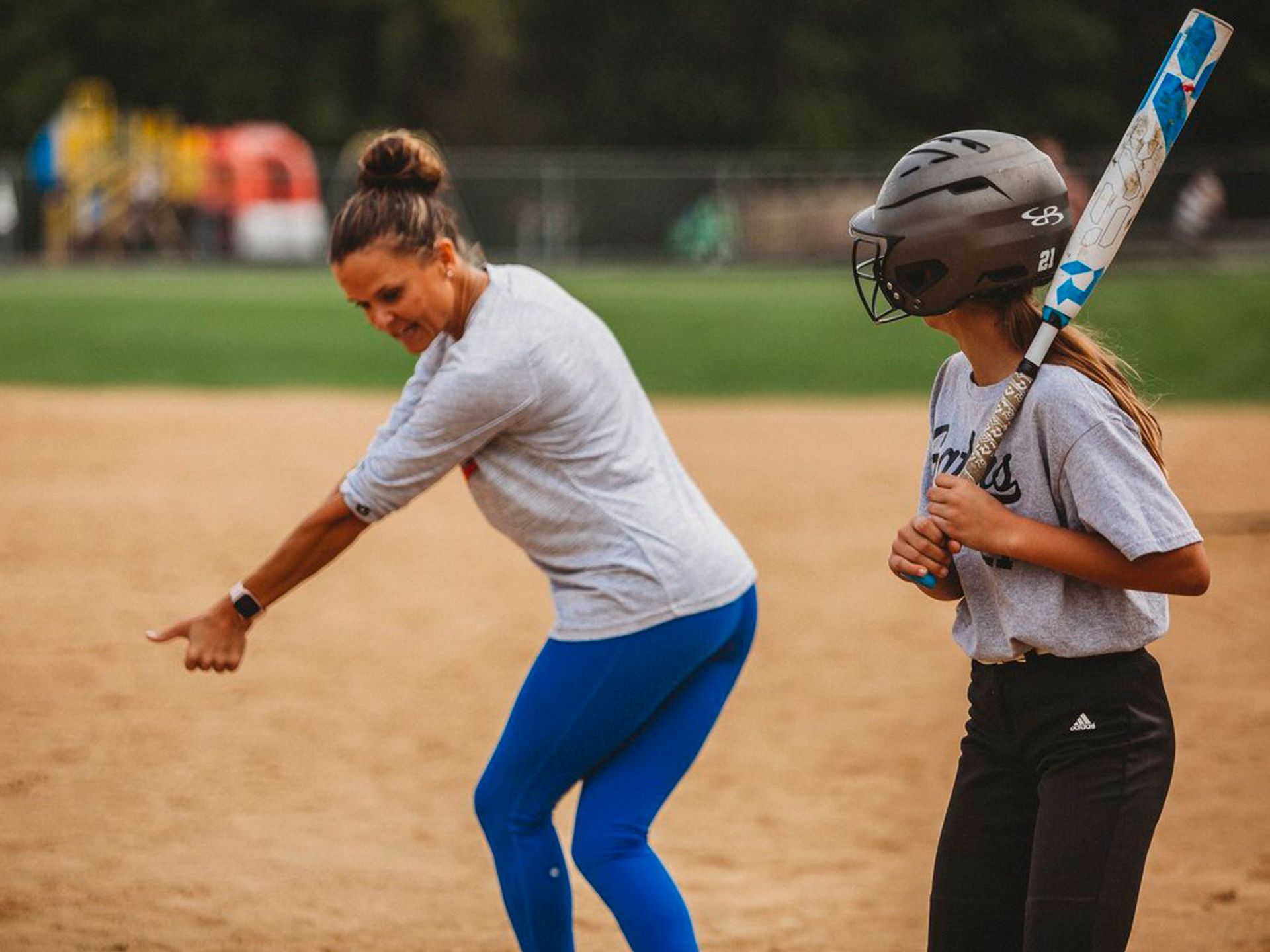 Coach YO is standing next to a girl holding a bat on a baseball field.