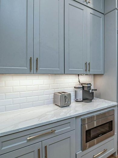 A kitchen with gray cabinets , white counter tops , stainless steel appliances and a microwave oven.