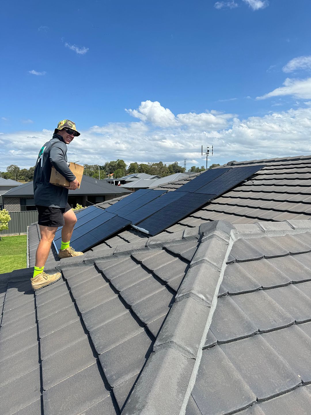 A Man Is Standing On Top Of A Roof Holding A Box — Rid-Arc Electrical In Tamworth, NSW