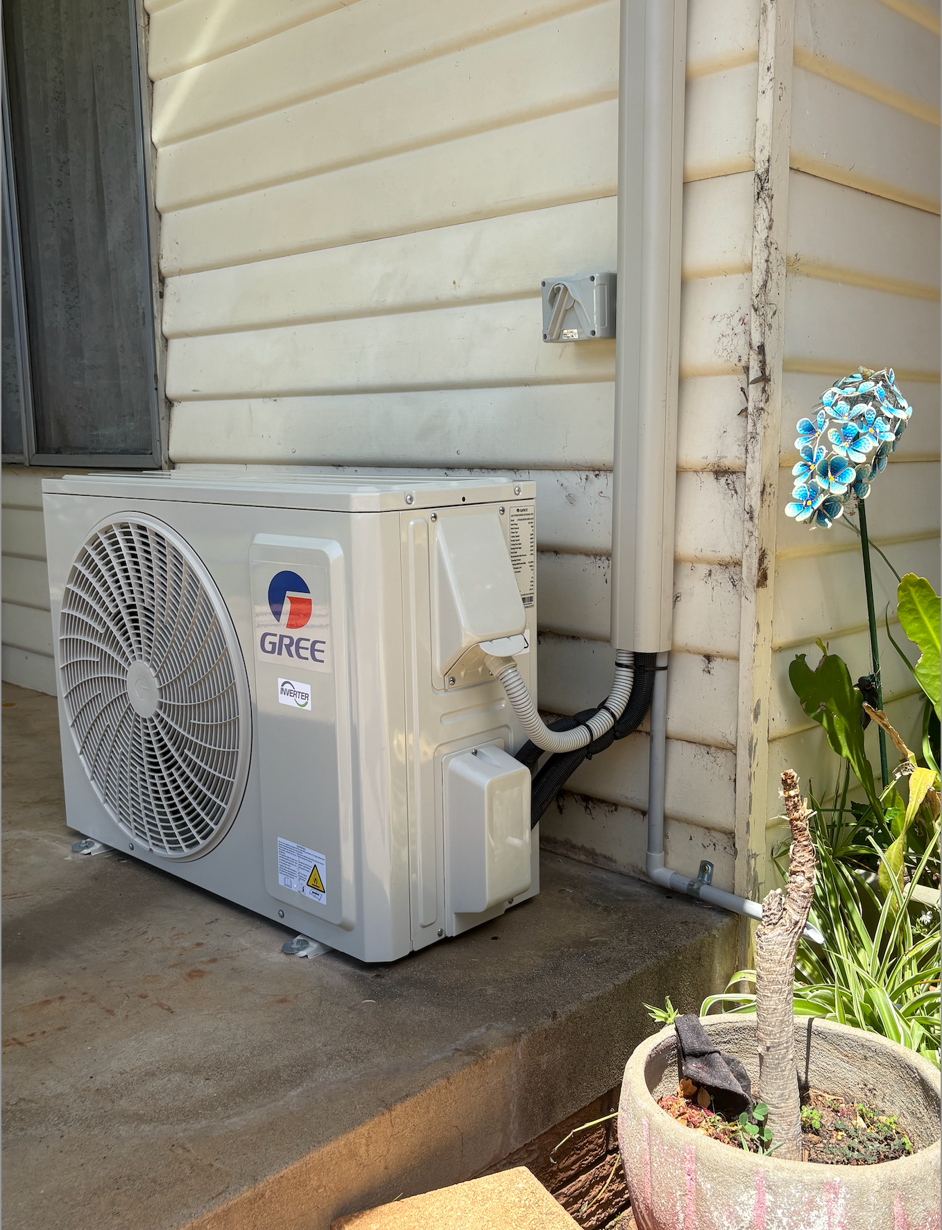 An Air Conditioner Is Sitting On The Side Of A House Next To A Potted Plant — Rid-Arc Electrical In Tamworth, NSW