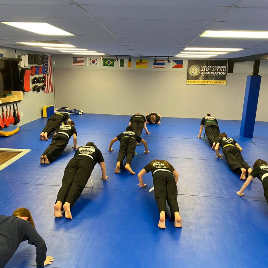 a group of people are doing push ups in a gym with a sign that says jiu-jitsu academy