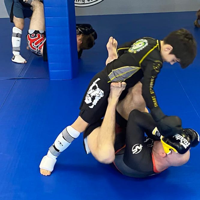 Two men are wrestling on a blue mat and one has the number 69 on his shorts