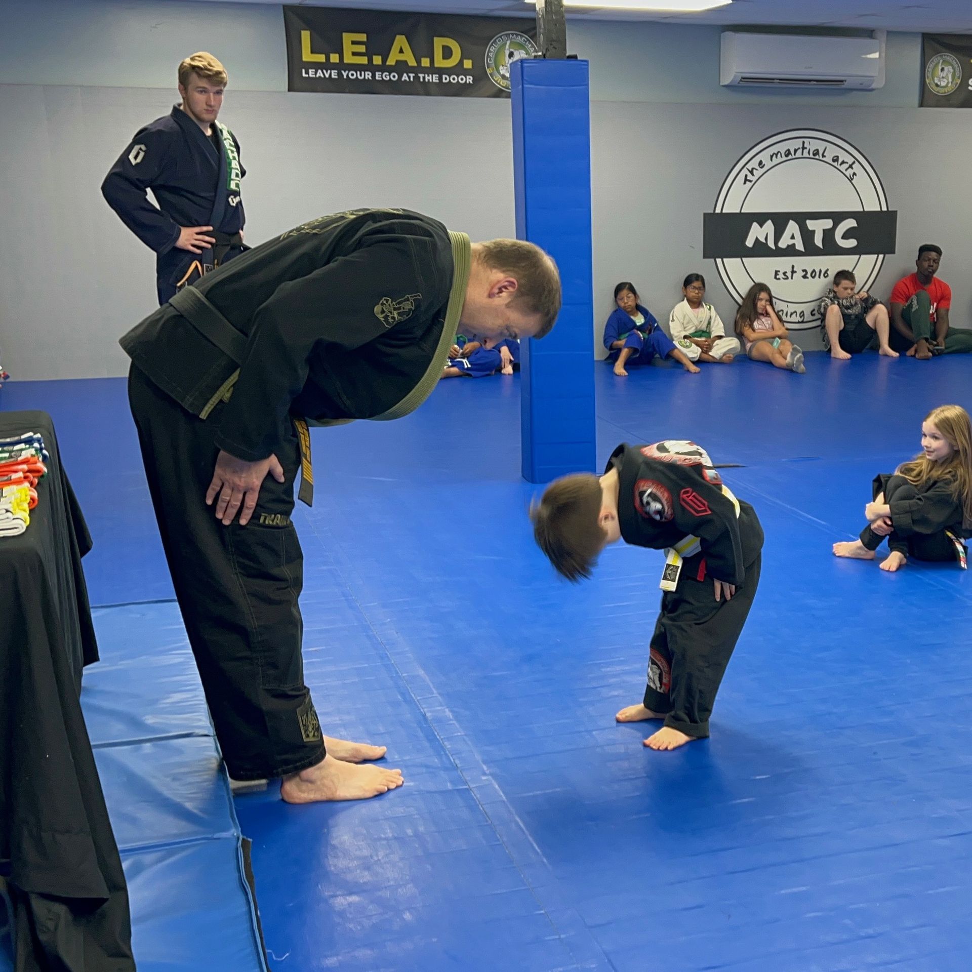 A man bows to a child in front of a matc sign