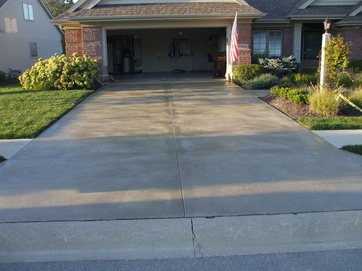 Wide concrete driveway leading to an open garage beside a suburban house