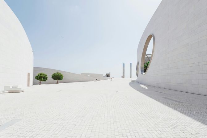 Bright white modern courtyard with curved walls, small trees, and a large oval window.