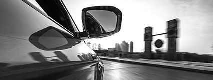 Ein Schwarzweißfoto eines Autos, das eine Stadtstraße entlangfährt.