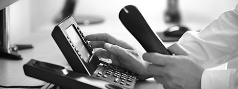 Eine Person hält ein Mobiltelefon neben einem Telefon.