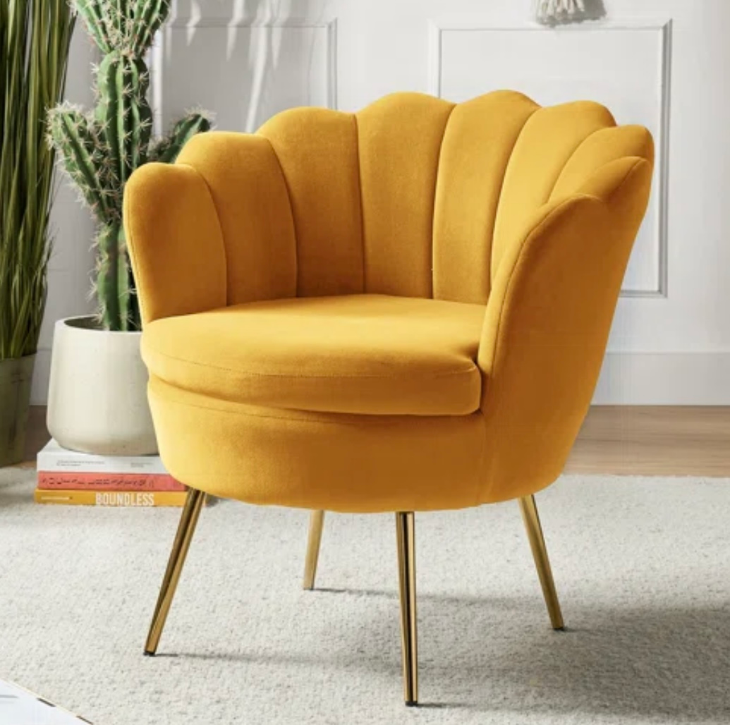 Yellow velvet accent chair with gold legs, against a soft-lit background with plants.