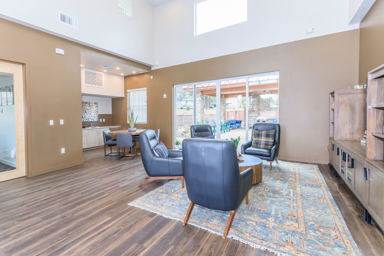 Modern apartment community lounge with seating, rug, and kitchenette; outdoor patio visible.